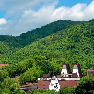 Suntory Yamazaki Distillery surrounded by lush green mountains under a blue sky.