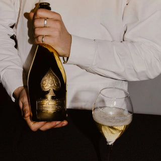Person holding a bottle of champagne with a glass nearby