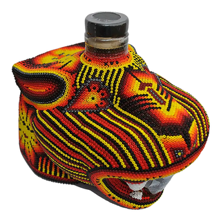 Chaquira Anejo Tequila 750ml comes in a decorative bottle shaped like an animal head, adorned with intricate red, yellow, and black bead patterns. The top of the head features the cap. The tequila inside offers notes of caramelized agave.