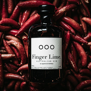 A dark glass bottle of Applewood Finger Lime Gin 500ml rests on red finger limes, its label lit to showcase this citrus gin crafted with native botanicals.