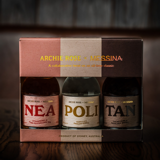 The Archie Rose x Messina Neapolitan Set—a boxed trio of NEA (strawberry gin), POLI (vanilla pandan vodka), and TAN (chocolate cacao hazelnut whisky)—is elegantly displayed on a wooden surface.