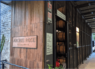 Archie Rose Distilling Co. sign on a wooden wall with barrels in the background