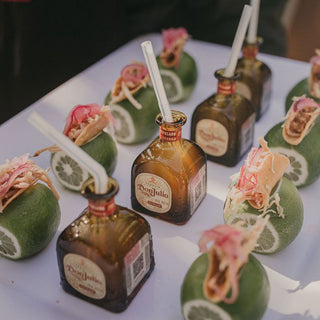 Don Julio Reposado Tequila 50ml bottles with straws are set inside hollowed limes, garnished with pickled onions and toppings on a white tray to showcase the honeyed agave spirit’s caramel and vanilla notes.