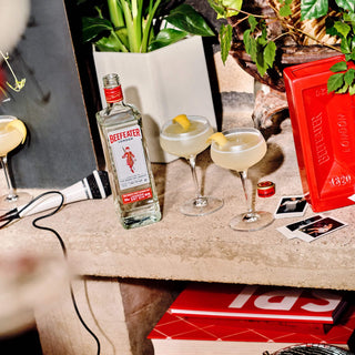 Bottle of Beefeater gin with cocktails on a bar counter, featuring the brand's red box.