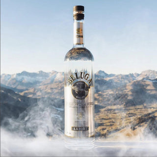 A clear Beluga Noble Russian Vodka 700ml bottle stands on a frosty surface with snow-capped mountains and a blue sky in the background, emphasizing its creamy texture and exceptionally smooth finish.