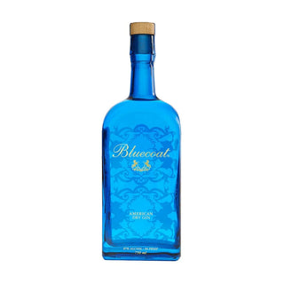 A 750ml blue glass bottle of Bluecoat American Dry Gin features gold lettering and decorative designs, showcasing its vibrant citrus and juniper botanicals, displayed against a white background.