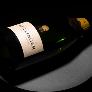 A bottle of Bollinger Special Cuvée Brut NV James Bond 007 Limited Edition rests sideways on a dark backdrop, with light accentuating its label and gold foil neck—an evocative image that suggests the champagne's full-bodied style.
