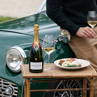 Bottle of Bollinger champagne with two glasses and a plate of food on a vintage car's hood.