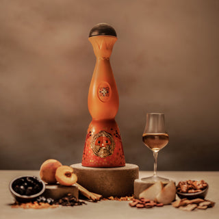 Clase Azul Dia de Los Muertos 2023 Aromas Limited Edition stands tall in an ornate orange bottle by a glass of amber liquid, surrounded by peaches, berries, nuts, and pear slices—suggesting vanilla caramel and toasted oak notes.