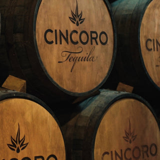 A close-up of stacked wooden barrels with the Cincoro Anejo Tequila 750ml logo and decorative designs, highlighting notes of toasted oak and caramelized agave.
