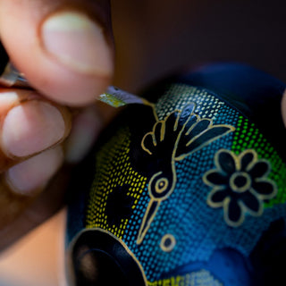 A close-up of a hand using a pointed tool to carve an intricate bird and flower design into the Clase Azul Mezcal Guerrero bottle, showcasing the honeyed sweetness of careful craftsmanship.