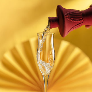 Clear liquid from a Clase Azul Mezcal San Luis Potosi 750ml red bottle is poured into a champagne flute, set against a pleated yellow background, hinting at smoky or herbal notes in the mezcal.