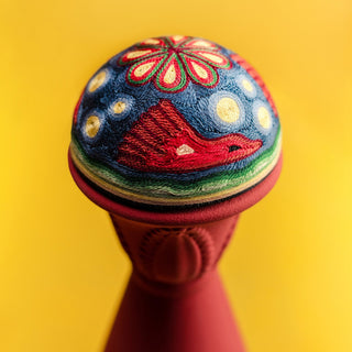 Clase Azul Mezcal San Luis Potosi 750ml features a vibrant, embroidered sphere with a red fox, yellow and white dots, floral patterns with smoky accents on top, set on a bright yellow background and a reddish stand.