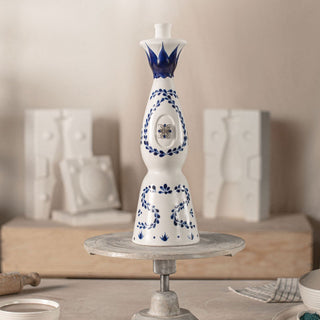 A blue and white Clase Azul Reposado Tequila 750ml bottle sits on a metal stand, its design evoking smooth vanilla tones.