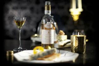 Bottle of white wine with a glass on a table with candles and food.