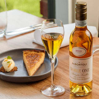 Bottle and glass of De Bortoli Noble One wine with dessert on a table