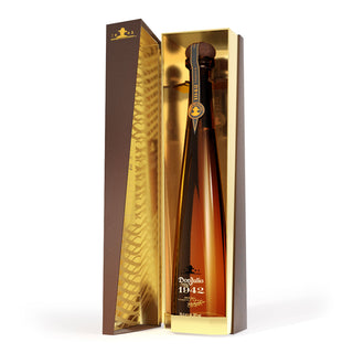 A tall, elegant bottle of Don Julio 1942 Añejo Tequila 750ml in a gold and brown gift box stands open, revealing the rich bottle inside. Notes of honeyed agave and vanilla echo the gold-lined interior and black-and-gold label.