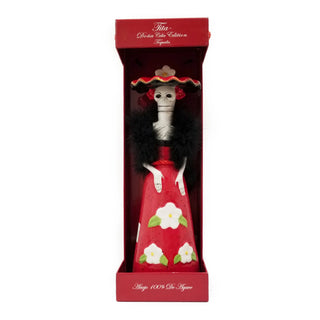 The Doña Celia Añejo Tequila 375ml comes in a red box with decorative text and features a ceramic Day of the Dead skeleton figurine dressed in red with white flowers, a black feather boa, and wide-brimmed hat—evoking caramel and vanilla notes.