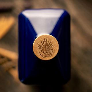A close-up of Don Fulano Imperial Extra-Añejo Tequila 700ml shows its blue bottle with a gold agave-embossed cap, viewed from above on wood, evoking rich agave flavors and subtle vanilla notes.