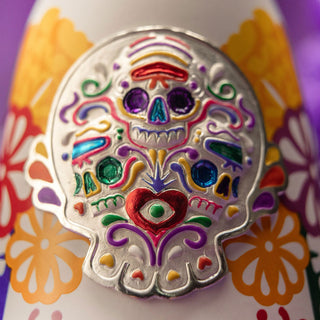 Close-up of the Clase Azul Dia de Los Muertos 2022 Colores Limited Edition Tequila 1L bottle, featuring a colorful embossed metal skull with vibrant patterns, a red heart, and floral motifs inspired by Day of the Dead art and fresh agave.