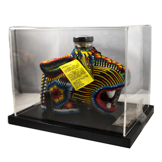 Chaquira Extra Anejo Tequila 750ml comes in a jaguar-shaped bottle adorned with vibrant beadwork, inspired by roasted agave. It’s displayed in a clear case with a black base and features a yellow tag hanging from the neck.