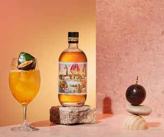Bottle of amaretto with a glass of amaretto cocktail and passion fruit on a pink background