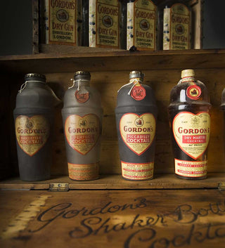 Collection of Gordon's gin bottles and packaging on a wooden shelf.