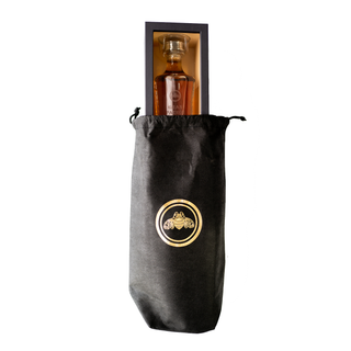 A 750ml glass bottle of Gran Patron Piedra Extra Anejo Tequila, in a rectangular box and partly covered by a black drawstring bag with a gold bee emblem, is shown on a white background, suggesting notes of caramel and dark chocolate.