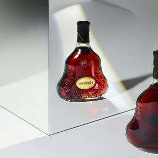 Two bottles of Hennessy cognac on a reflective surface with a neutral background