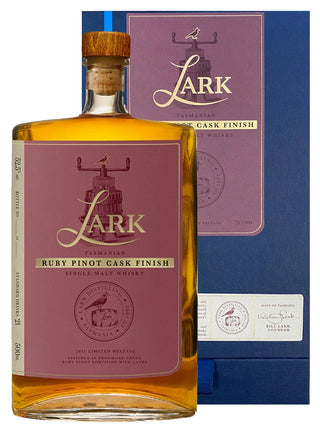 A bottle of Lark Ruby Pinot Cask Finish single malt whisky with a dusty rose label and cork stopper, shown in front of its blue and mauve gift box on a white background.