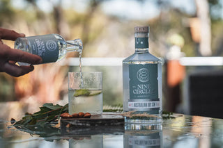 Person pouring Nine Circle gin into a glass with a blurred outdoor background