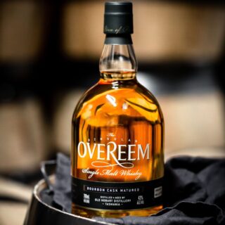 A bottle of Overeem Bourbon Cask Matured – Distiller’s Strength Tasmanian Single Malt Whisky rests on dark cloth, warm light enhancing the amber liquid and inviting aromas of vanilla caramel.