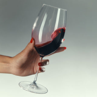 Hand holding a glass of red wine against a gray background
