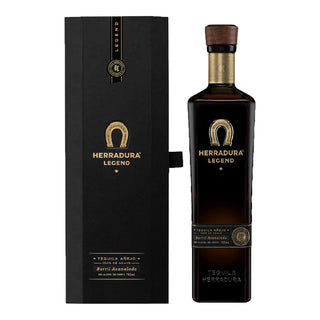 A black gift box and a tall, dark bottle of Herradura Legend Anejo Tequila 750ml feature gold accents and a horseshoe logo. The wood-style stopper tops tequila with toasted oak and vanilla notes.
