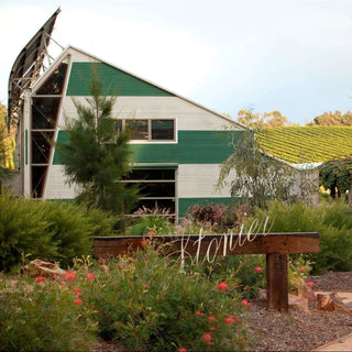 Green barn with a wooden sign in front, surrounded by greenery