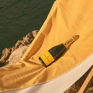 Bottle of Veuve Clicquot champagne on a yellow towel by the sea.